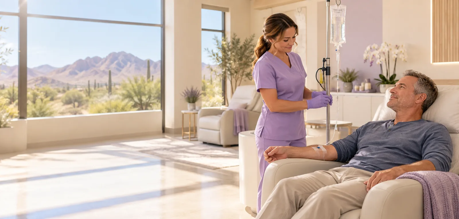 A client receiving a DMSO infusion in a recliner while a nurse adjusts the line, with a desert view, in Mesa, Arizona