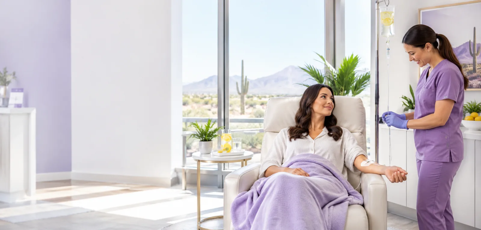 A client receiving an IV vitamin C infusion in a recliner while a nurse adjusts the line, with a desert view, in Mesa, Arizona